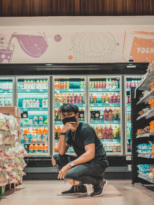 Free Man in mask hunkering down near supermarket shelves Stock Photo