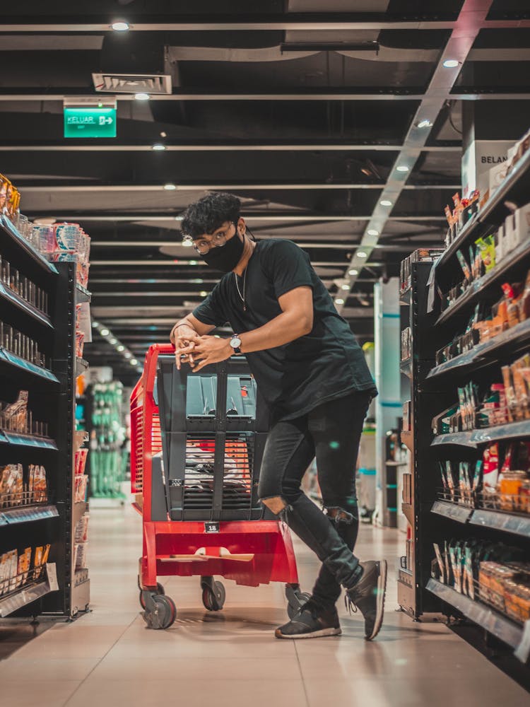 Confident Man In Mask Leaning On Trolley In Supermarket