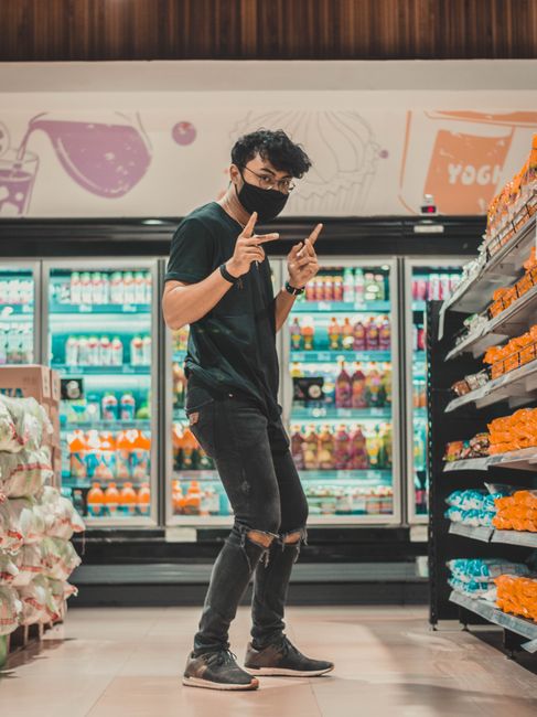 Full length young positive male in ripped jeans and face mask dancing amidst shelves in modern grocery store and looking at camera Full length young positive male in ripped jeans and face mask dancing amidst shelves in modern grocery store and looking at camera