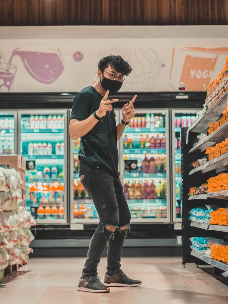 Young Man In Mask Dancing Near Supermarket Shelf