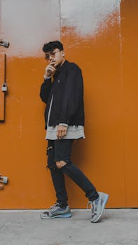 Young man with a confident pose wearing street style fashion against an orange backdrop.
