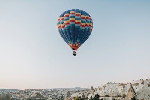Picturesque scenery of colorful hot air balloon soaring above spacious rocky terrain against cloudless blue sky in early morning