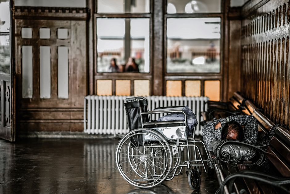 Un hombre cansado durmiendo en un banco al lado de una silla de ruedas en la histórica estación de tren de Estambul.