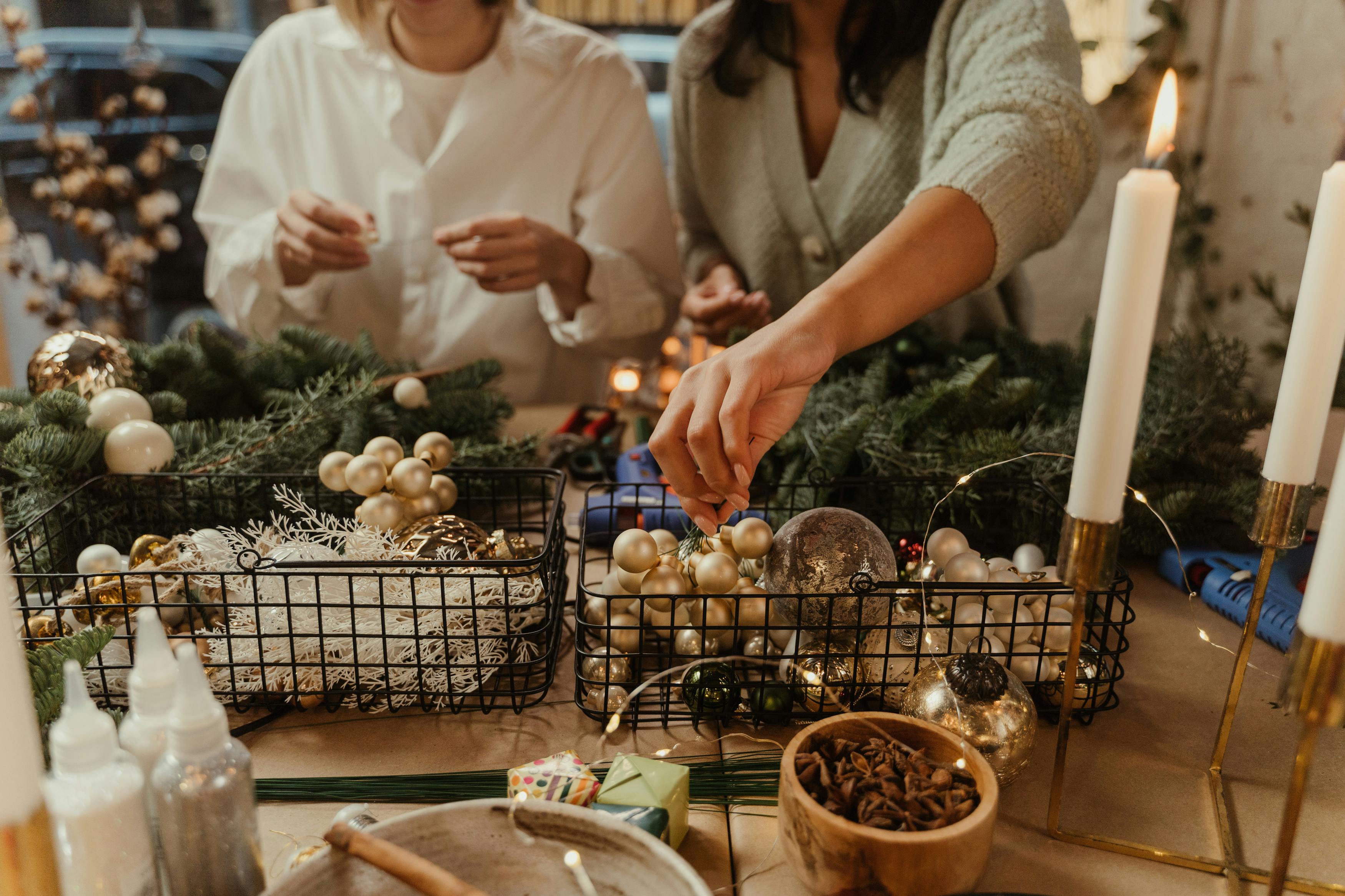 People crafting Christmas decorations with ornaments and candles indoors.
