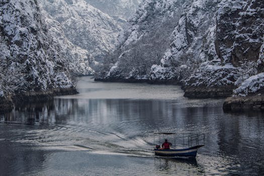A solitary boat navigates a snow-covered gorge, creating a serene winter landscape.
