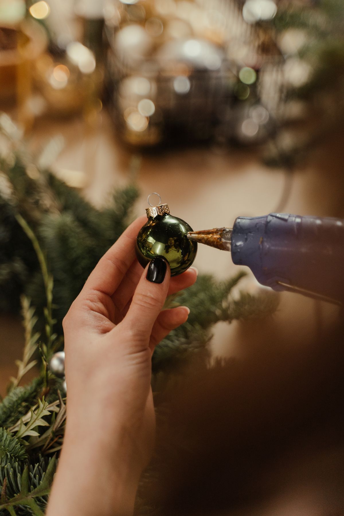 Hand using a glue gun on a green ornament among conifer branches and pinecones