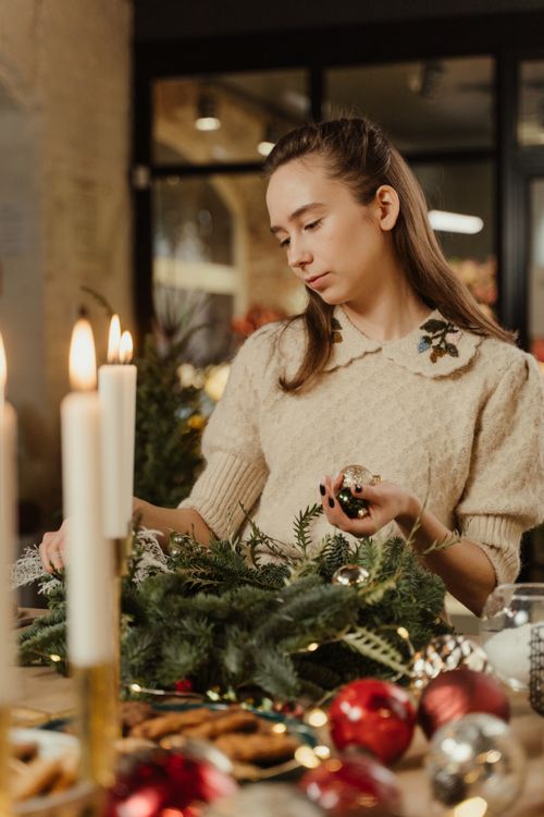 Free Woman crafting a Christmas wreath on a table with candles and ornaments. Stock Photo