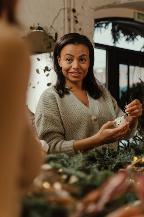 A Woman in Gray Knitted Sweater Holding a Silver Christmas Ball 