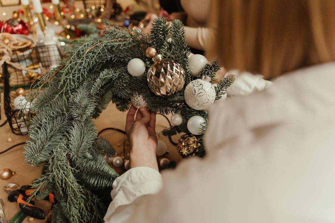 Hands attaching evergreen branches and ornaments to a Christmas wreath