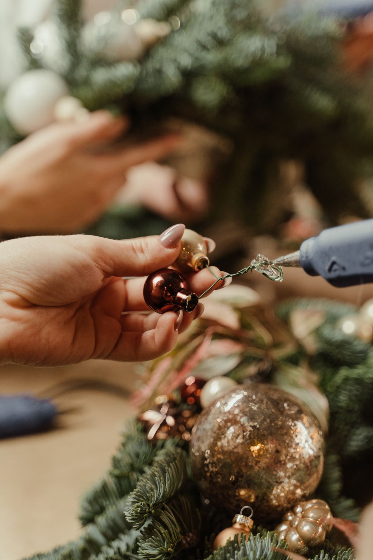 Hands crafting a Christmas wreath covered in baubles using a glue gun