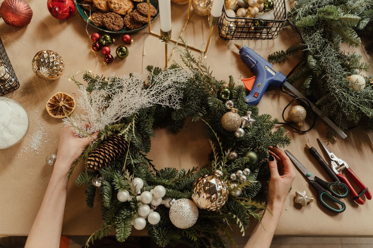 Hands crafting a holiday wreath with pinecones and greenery on a wooden table