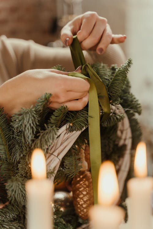 A Person Putting Green Ribbon on the Christmas Wreath