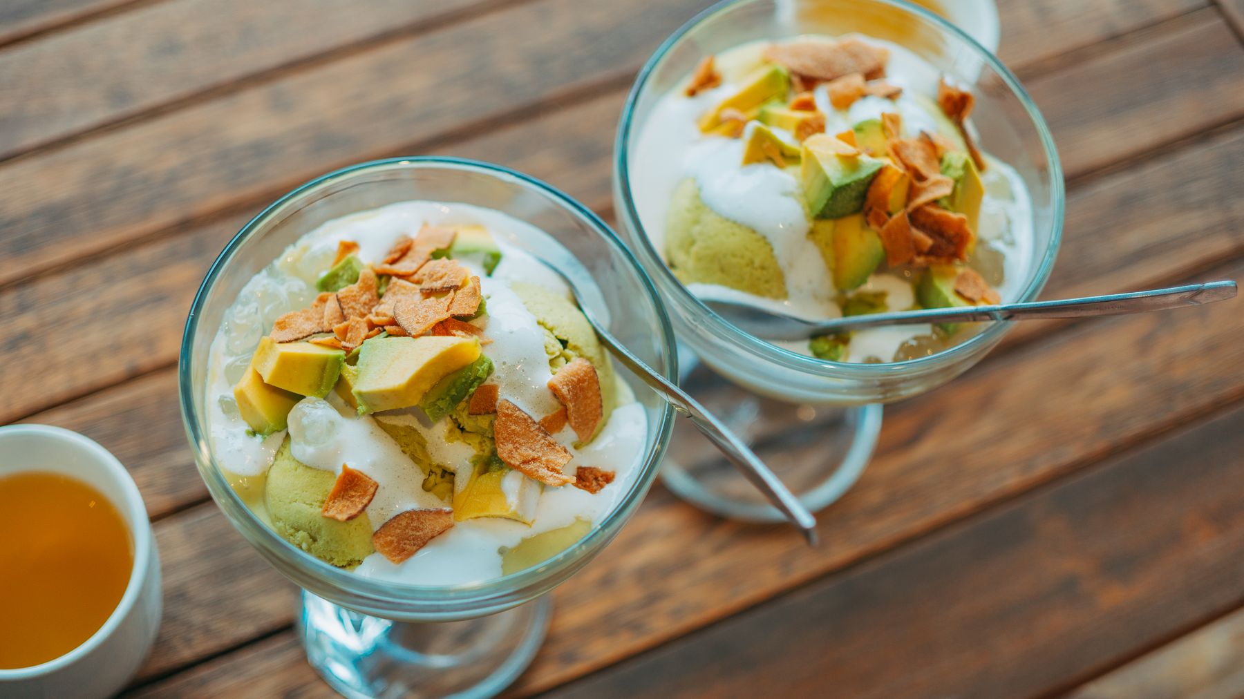 Top view of avocado dessert with cream in glass bowls on wooden table.