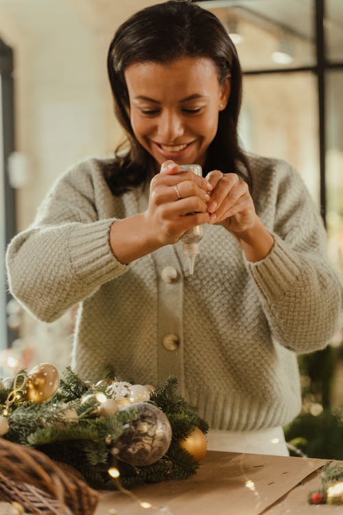 Woman in Knitted Sweater Smiling While Decorating a Christmas Wreath