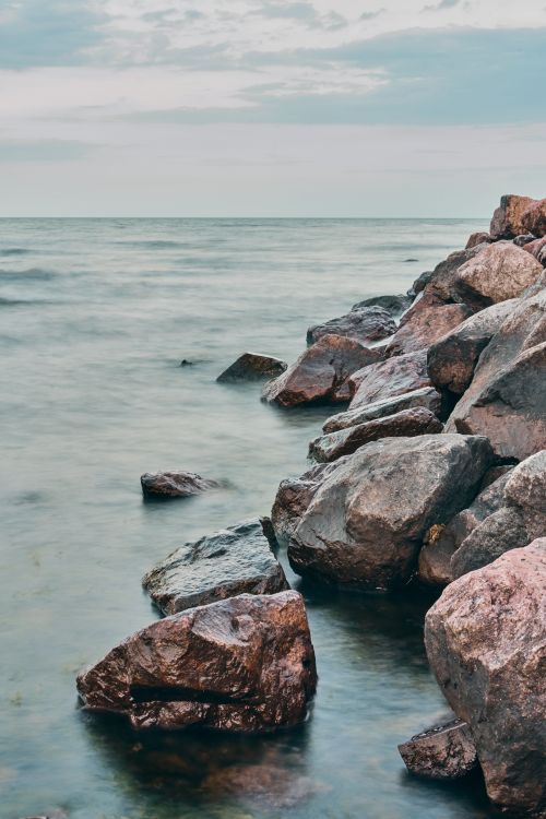 Free Tranquil seascape of rocky shoreline and gentle waves under a cloudy sky. Stock Photo