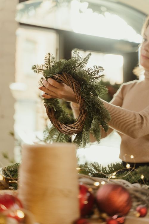 Free A woman creating a festive Christmas wreath with pine and ornaments indoors. Stock Photo