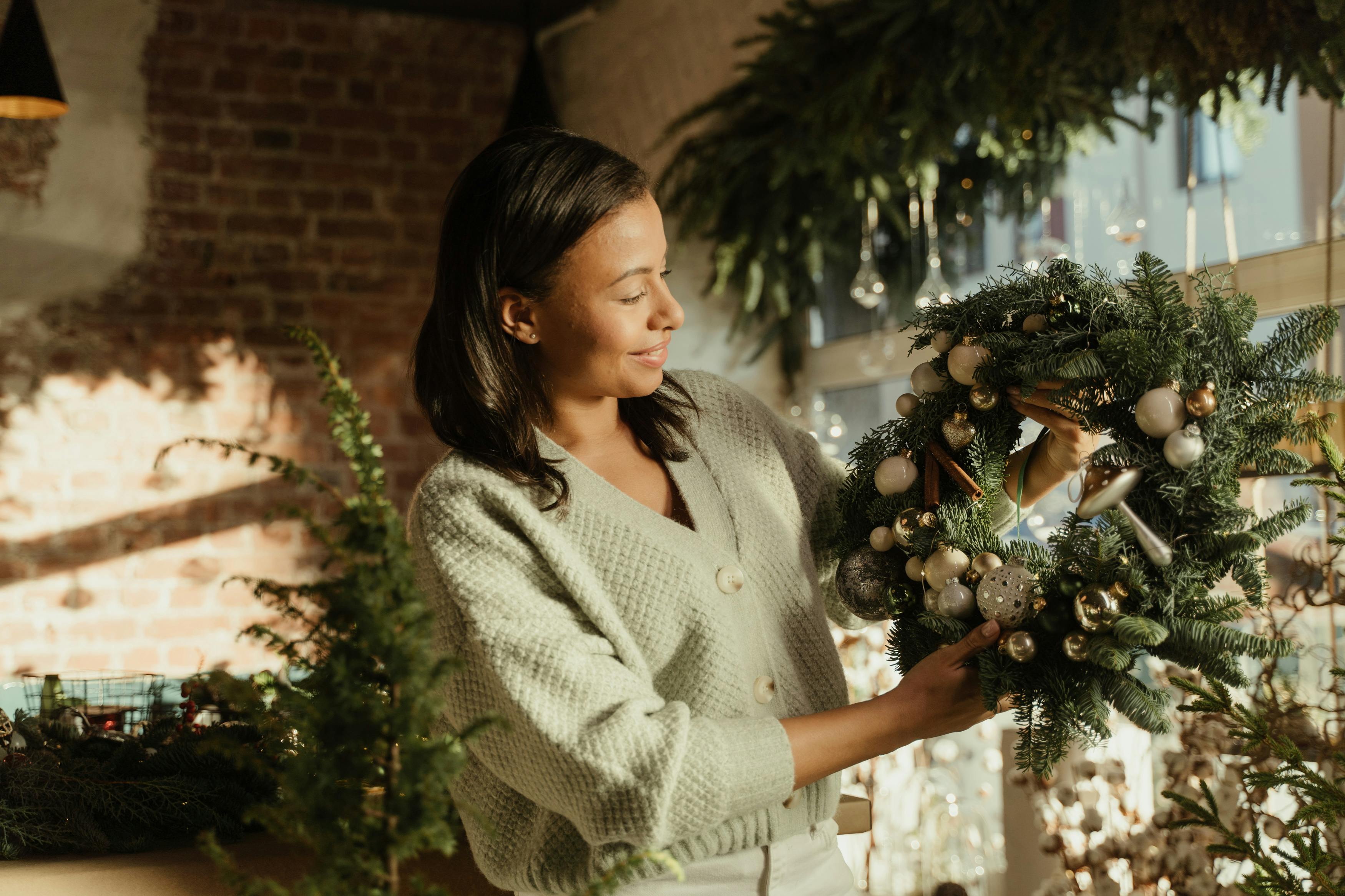 A woman admires a decorative Christmas wreath in a brightly lit room with festive holiday decor.