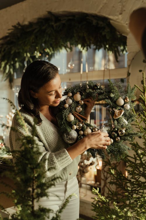 Woman in Gray Sweater Looking at the Christmas Wreath she is Holding