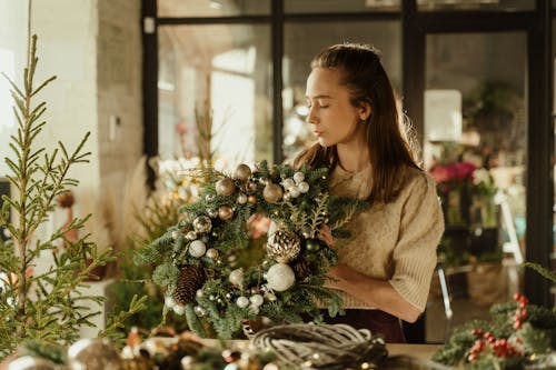 Woman in Brown Sweater Holding a Wreath with Christmas Balls