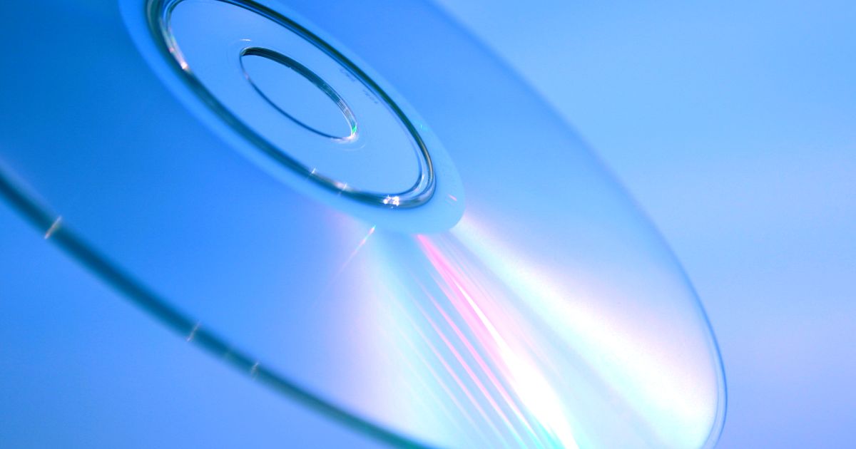 Detailný záber na CD s dúhovým odleskom na modrom pozadí.
