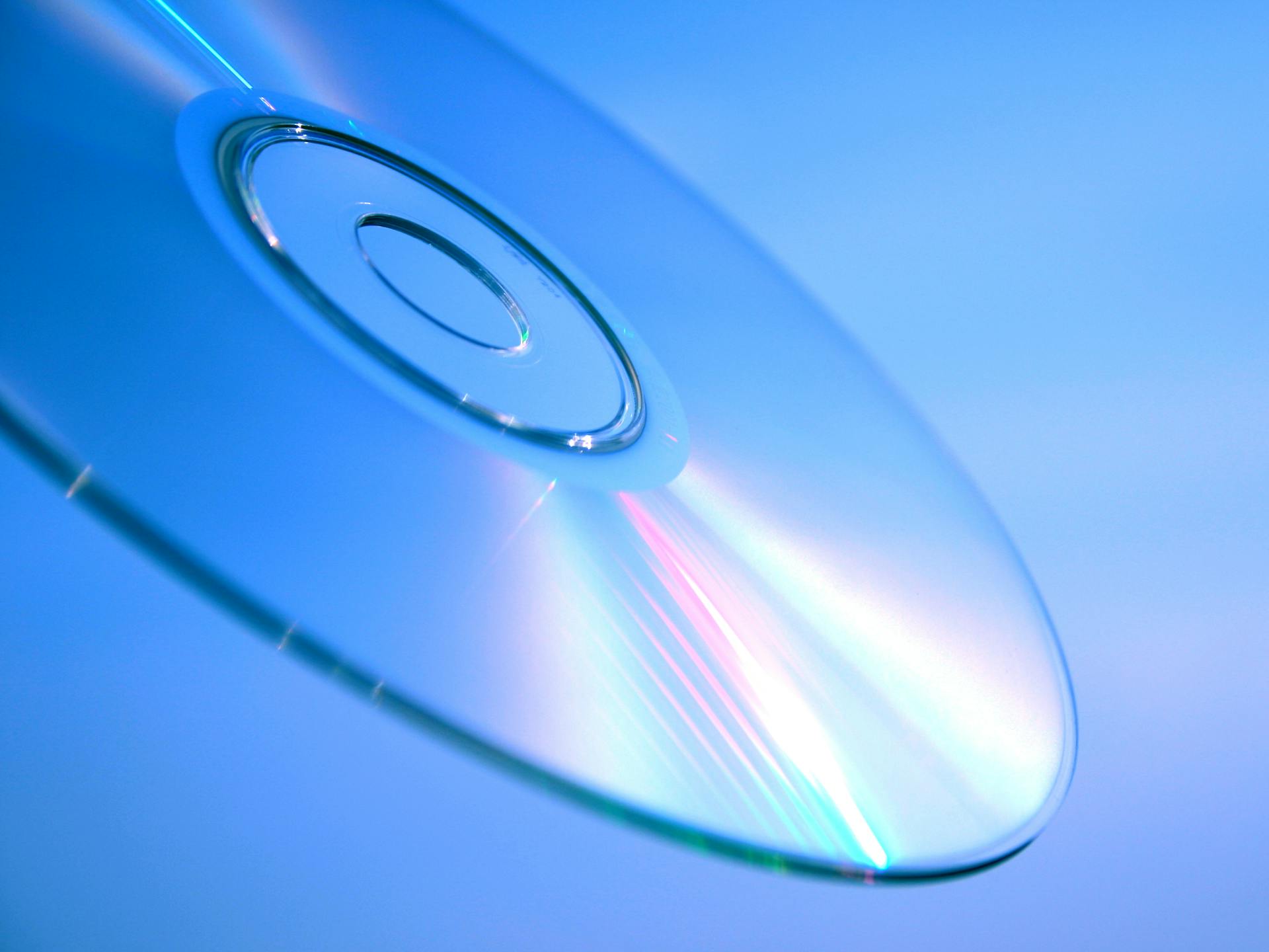 Detailed close-up of a reflective CD disc with rainbow hues and blue background.