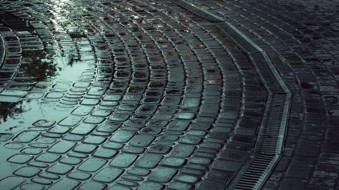 A wet street surface with standing water in the puddles