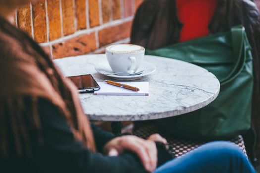 Warm scene of coffee and notepad in cozy cafe setting with visible smartphone.