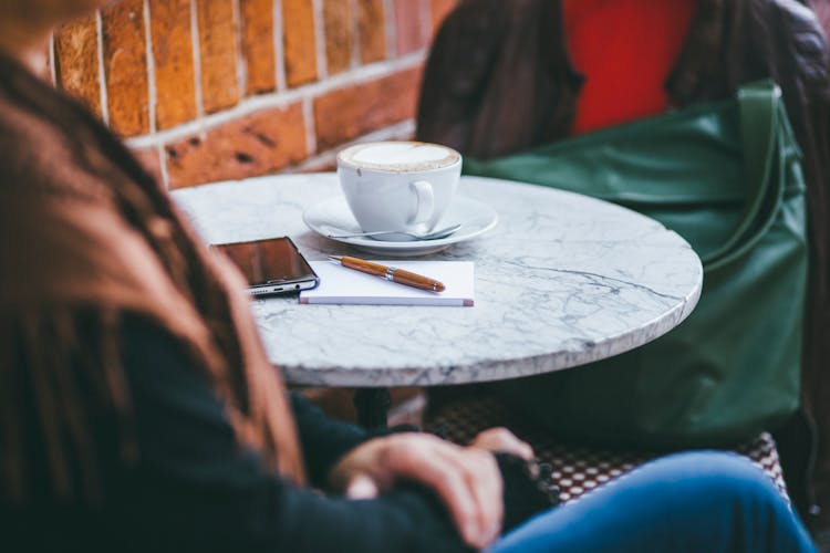 A Cup Of Cofee Near A Pen, Paper, And Smartphone On A Table