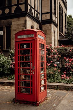 Vintage red telephone booth in London surrounded by flowers on a sunny day.