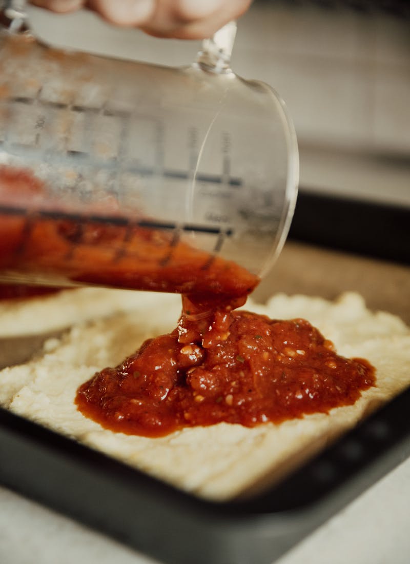 Clear Glass Jar Pouring Red Sauce Pizza Crust