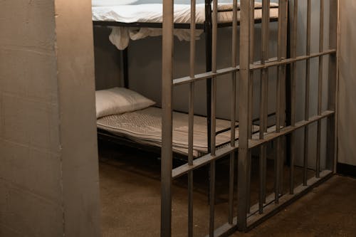 A Bunk Bed With Striped Linen Behind Bars