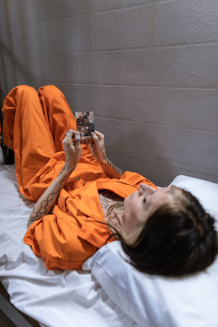 A Woman Wearing Prison Uniform Holding A Photo While Lying On Bed