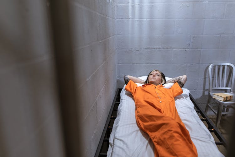 Woman In Orange Prison Uniform Lying On Bed