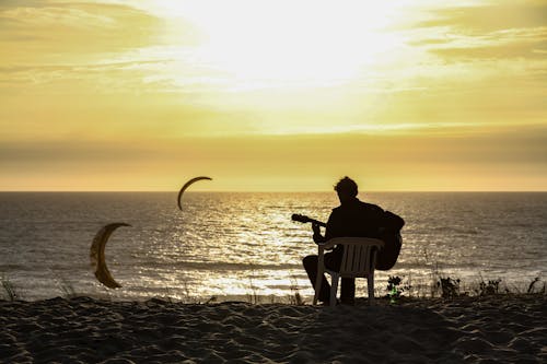 Free Silhouette of Man Sitting on Chair on Beach during Sunset Stock Photo