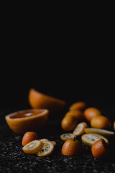 Vibrant kumquats sliced on a textured dark surface, highlighting citrus freshness and rustic appeal.