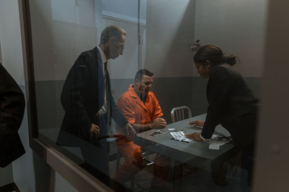 A tense interrogation in progress with a handcuffed inmate and two officers in a prison room.