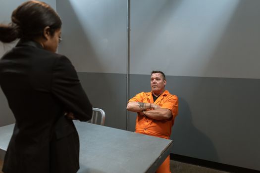 A Man in Prison Uniform Sitting Near the Table while Talking to the Officer in Black Blazer