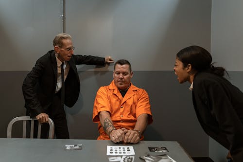 Free A Man in Orange Shirt Sitting Between the Officers Shouting at Him Stock Photo