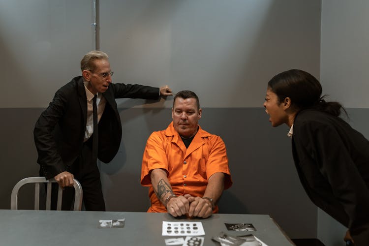 A Man In Orange Shirt Sitting Between The Officers Shouting At Him