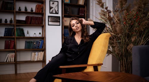 Stylish woman in black clothes sitting gracefully on armchair