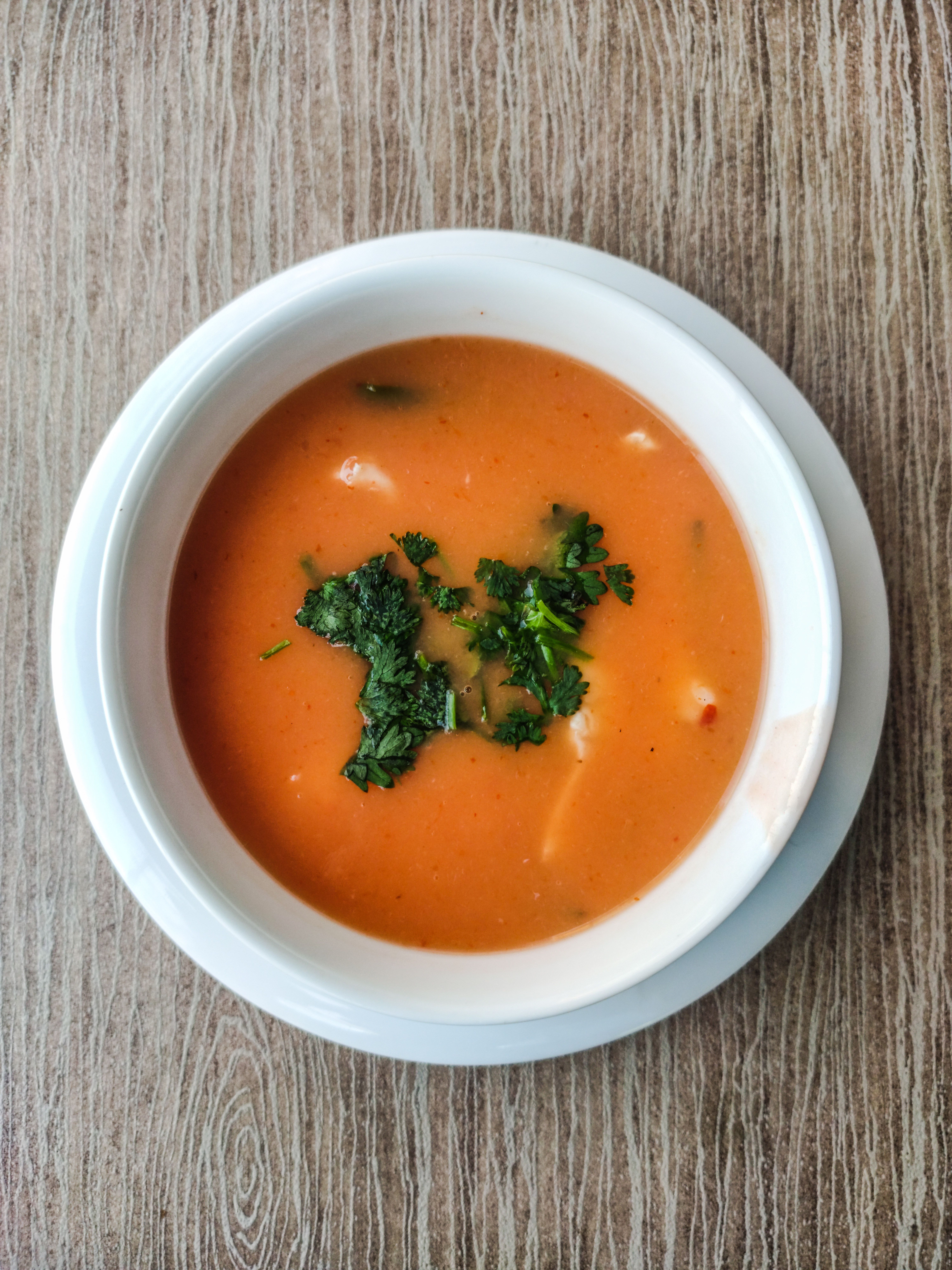 Aerial view of vibrant tomato soup garnished with fresh herbs in a white bowl.
