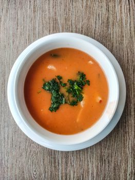 Aerial view of vibrant tomato soup garnished with fresh herbs in a white bowl.