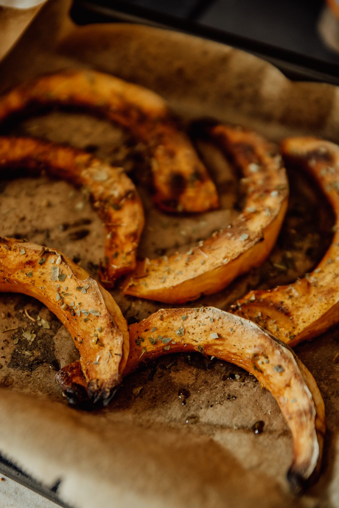 Roasted pumpkin wedges with herbs on a parchment-lined baking tray