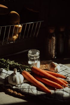 Moody kitchen composition featuring fresh carrots, garlic, and spices on a cloth.