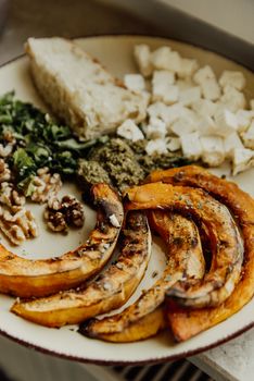 A rustic plate featuring roasted pumpkin slices, herbs, nuts, cheese, and bread, perfect for a cozy autumn meal.