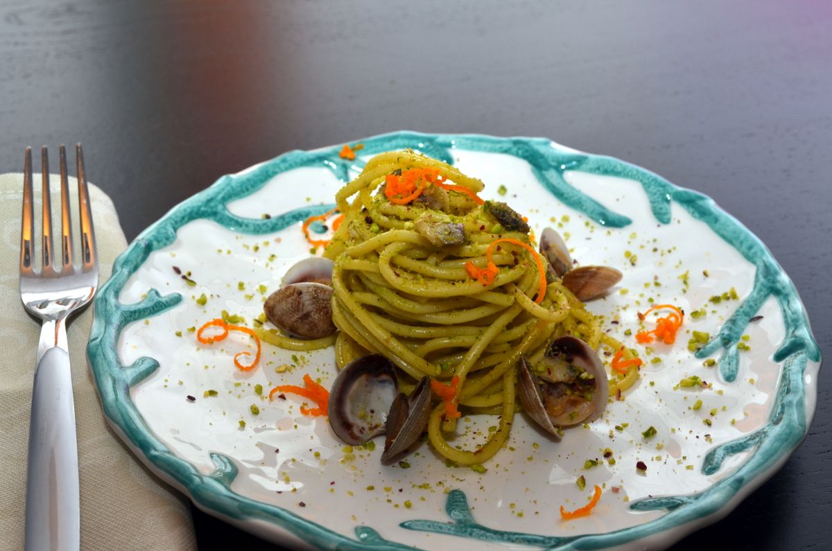 Pasta con vongole e granella di pistacchio in un piatto dal bordo turchese