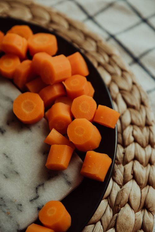 Free Freshly sliced carrot rondelles on a ceramic plate atop a woven tray. Perfect for culinary themes. Stock Photo