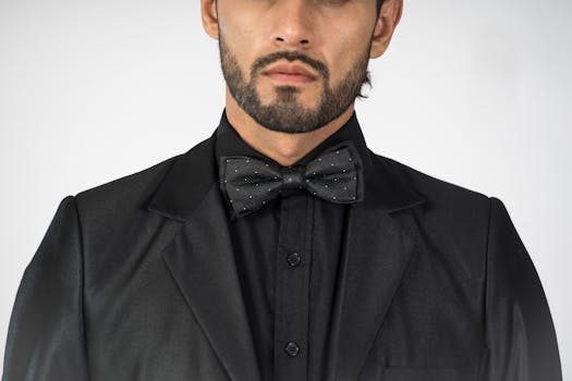 A stylish and well-dressed man wearing a black suit and bow tie in a studio setting.