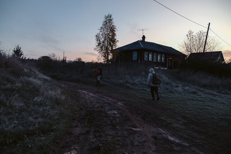 Unrecognizable People Walking On Dirt Road Near Rural House