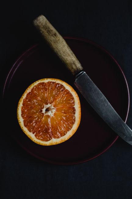 Vibrant sliced orange next to a rustic knife on a dark plate, perfect for fresh food themes.